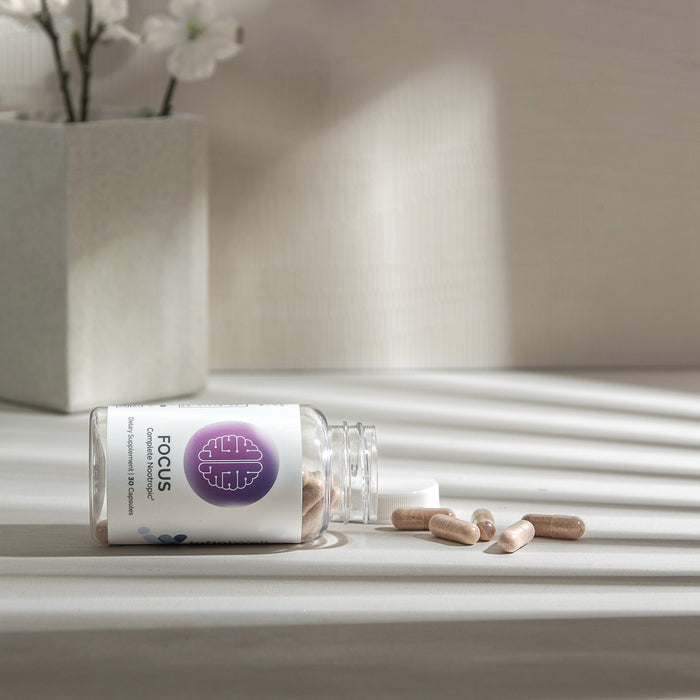 InfiniWell Focus Complete Nootropic dietary supplement bottle with spilled capsules on a white surface in natural light, 30 capsules.