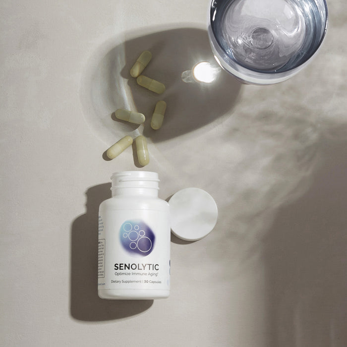Infiniwell Senolytic optimize immune aging supplement bottle with loose capsules, open cap and glass of water above