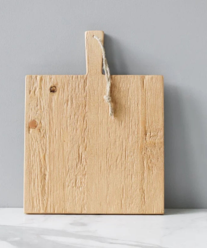 Square pine wood cutting or charcuterie board with a natural finish, featuring a dark horizontal stripe and a handle with a rope loop styled with cheese and wine.