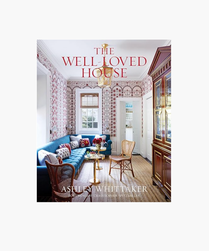 Cover of "The Well-Loved House" by Ashley Whittaker. Features a vibrant living room with a blue sofa, colorful pillows, patterned wallpaper, and a gold chandelier. | Wildwood Home Co.