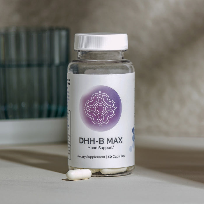 Infiniwell DHH-B MAX Mood Support supplement bottle with 30 capsules and loose capsule on light textured surface