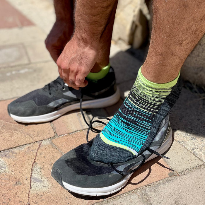 Ankle compression sock with a gradient design is worn while tying shoelaces on a running shoe.