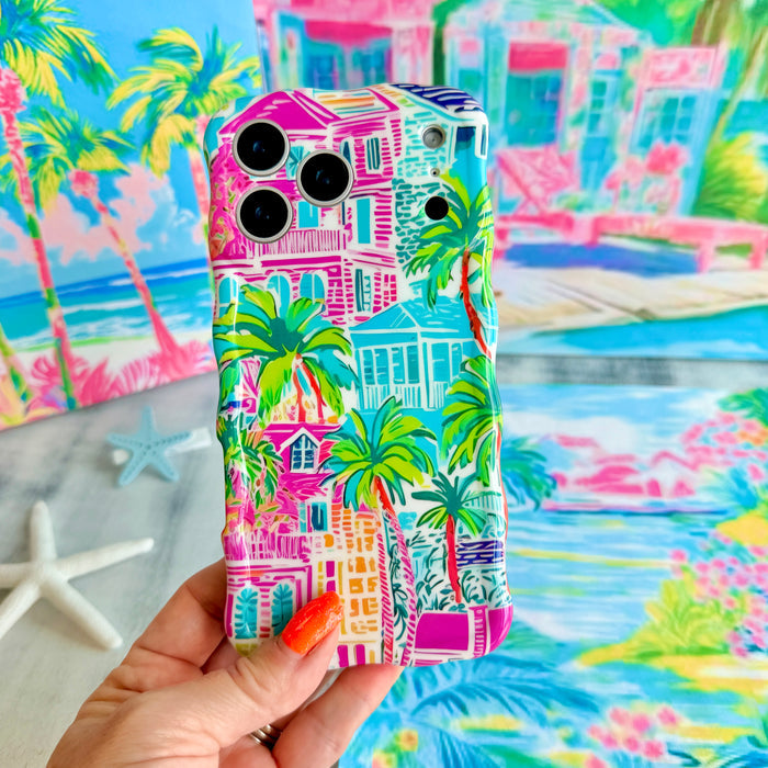 Trendy wavy iPhone case featuring a vibrant tropical resort scene with pink villas and green palm trees with a high-gloss finish.