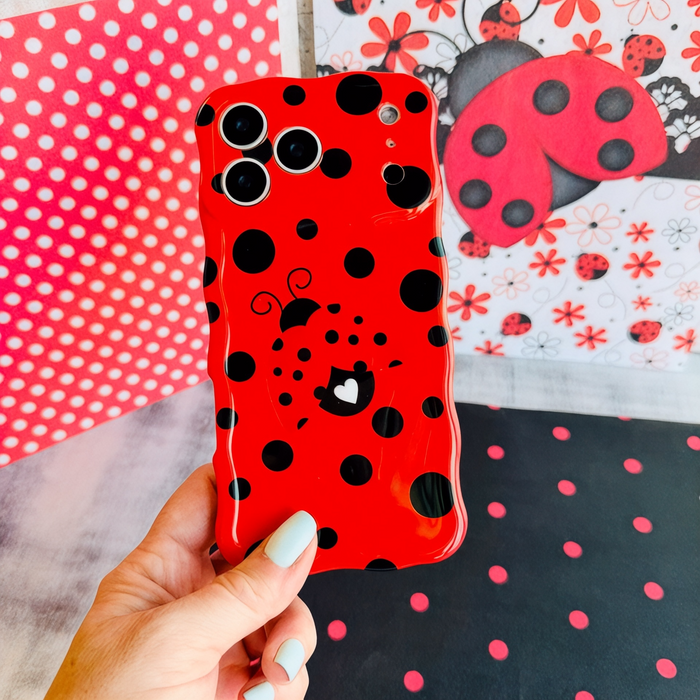 Bright red wavy iPhone case with large black polka dots and a central ladybug featuring a white heart on its wing.