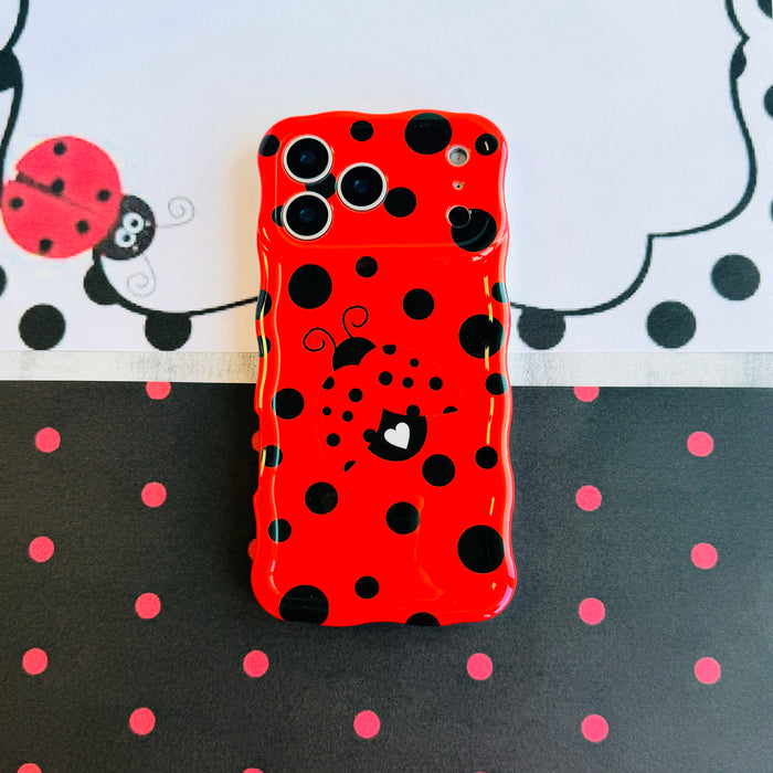 Bright red wavy iPhone case with large black polka dots and a central ladybug featuring a white heart on its wing.