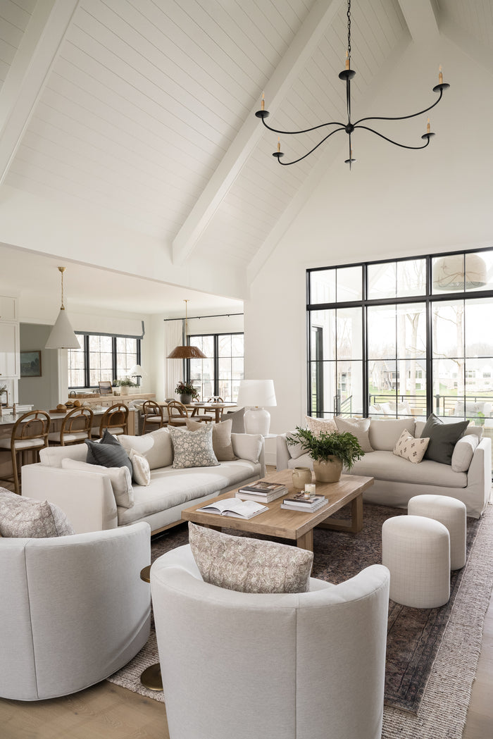 Spacious living room with plush white sofas, a wooden coffee table, and cozy armchairs. Large windows provide natural light, conveying a serene atmosphere. | SW Home