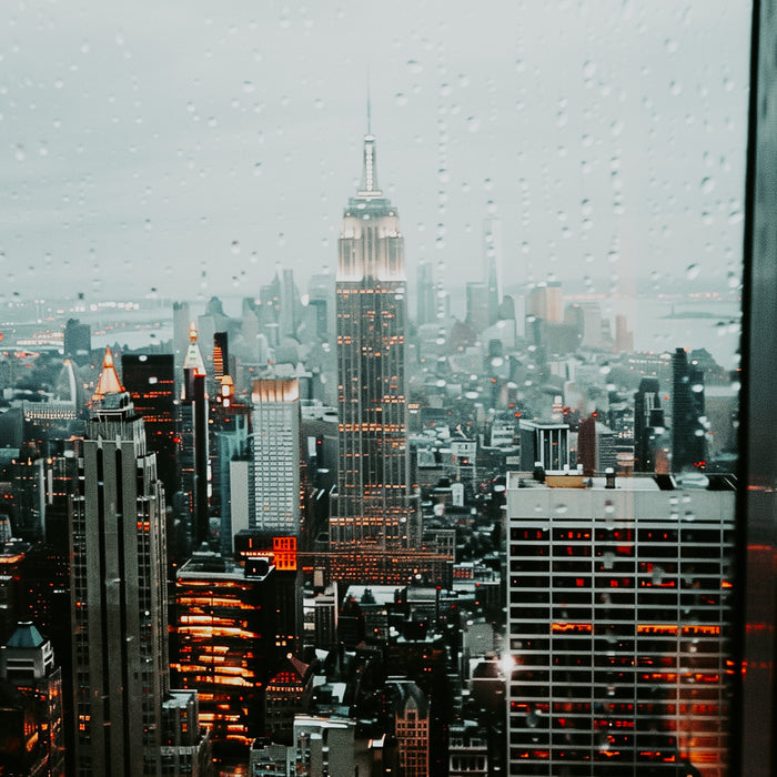A cityscape with high-rise buildings, including the Empire State Building, during a rainy day, viewed from a high vantage point.
