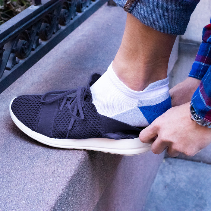 Ankle compression sock with a blue and white design being put on with a black sneaker on a stone surface.
