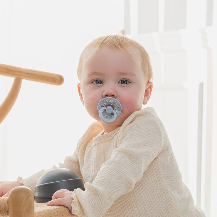 Baby with a pacifier sitting in a chair with a white curtain background