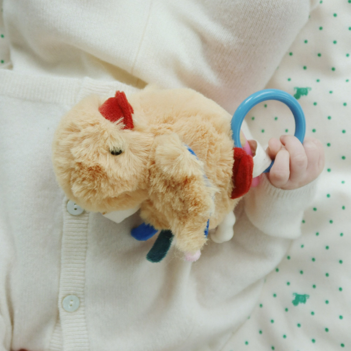 Child holding a plush toy with a blue ring, wearing a white sweater with green polka dots.