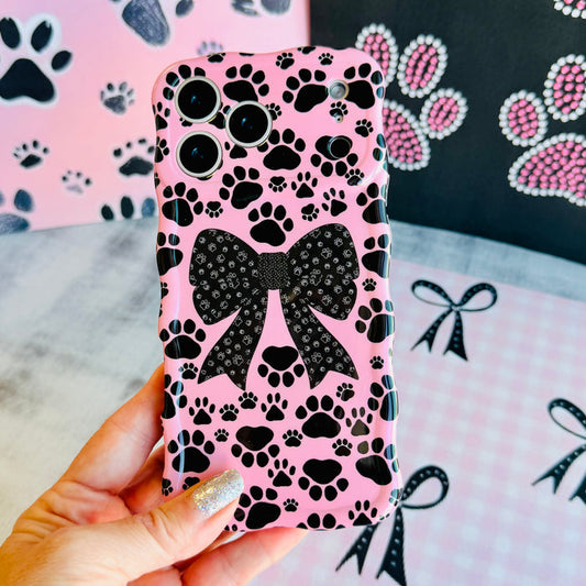 Trendy pink wavy iPhone case featuring a pattern of black paw prints and a large central black bow with tiny paw print details.