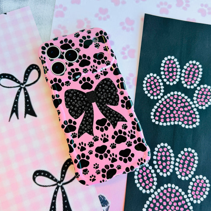 Trendy pink wavy iPhone case featuring a pattern of black paw prints and a large central black bow with tiny paw print details.