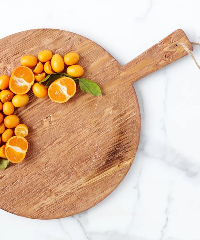 A round pine wood cutting board with a smooth surface and natural grain. It has a handle with a rope loop for hanging, conveying a rustic charm styled with sliced oranges.  | SW Home