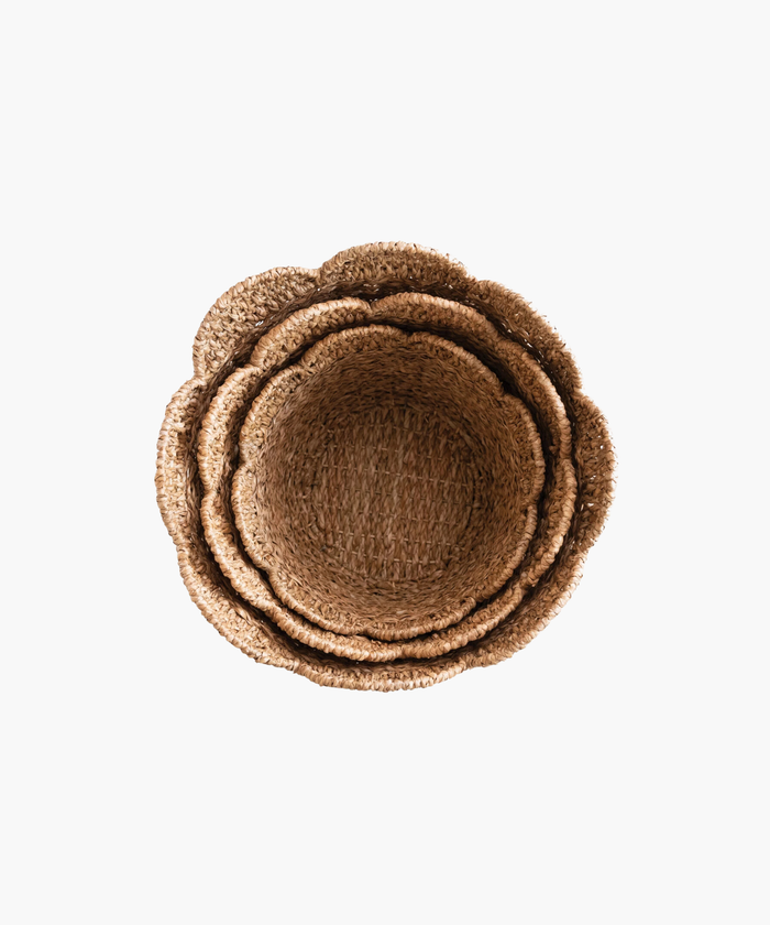 Overhead view of woven baskets in various sizes showing their scalloped edge in natural straw color. The texture is coarse, conveying a rustic and earthy tone. | Wildwood Home Co.