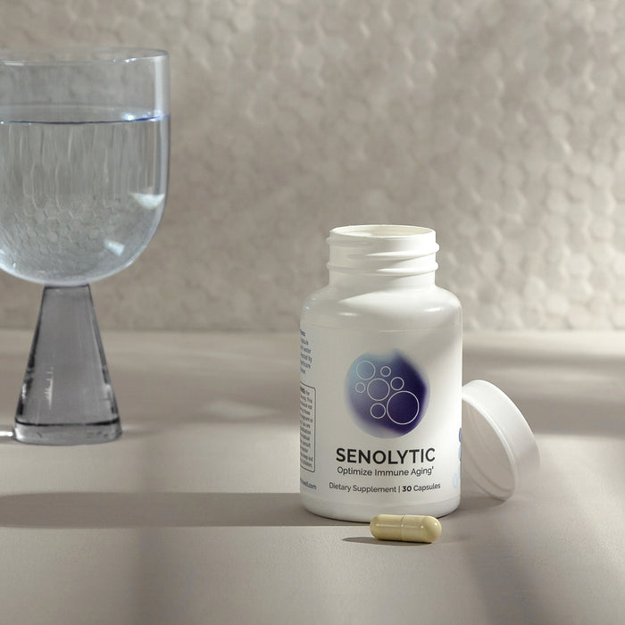 Infiniwell Senolytic optimize immune health supplement bottle with open cap, capsule and glass of water nearby
