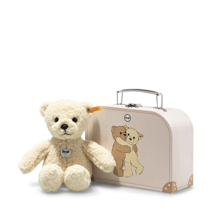 A vanilla-yellow teddy bear next to a pink suitcase with a graphic of two bears hugging on the side.